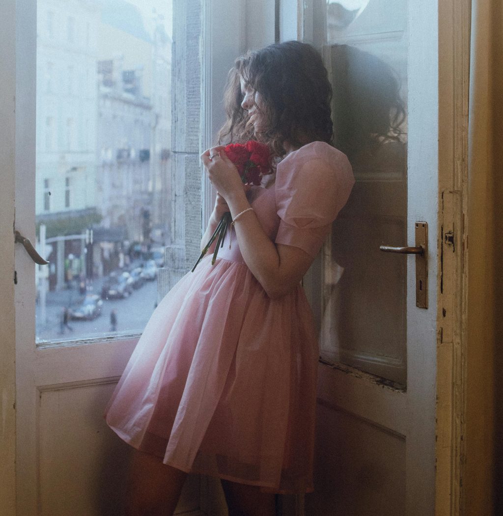 Photo by Tatyana Doloman: https://www.pexels.com/photo/young-woman-in-pink-dress-by-window-with-flowers-30538797/